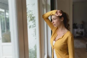 A woman standing by a window, gazing outside.