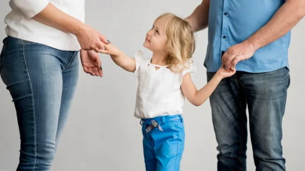 "A girl is holding her parents' hands while looking at her mother.
