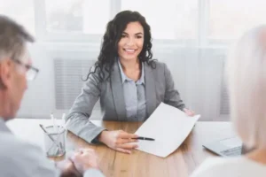 A woman is looking at the couple while showing them a paper and holding a pen.