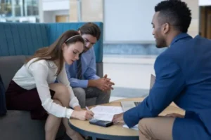 A woman is signing a document while her husband and lawyer are looking at her.
